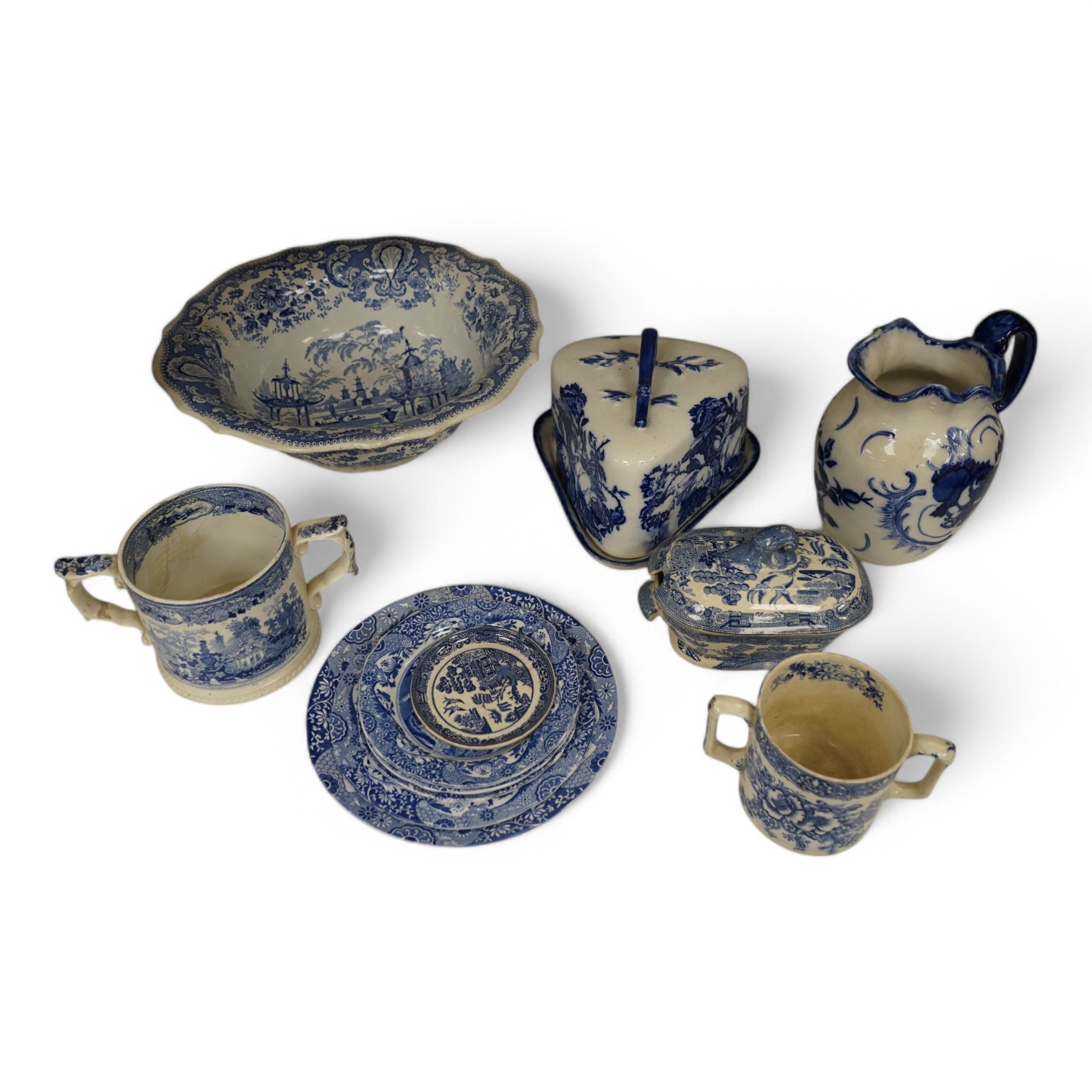 A group of blue and white ceramics to include Ironstone cheese dome and jug, a basin and twin handled cups, largest 36cm in diameter. Condition - varies